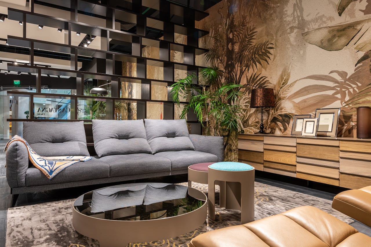 Stylish living room featuring a plush sofa, mirrored table, and tropical-themed wallpaper.